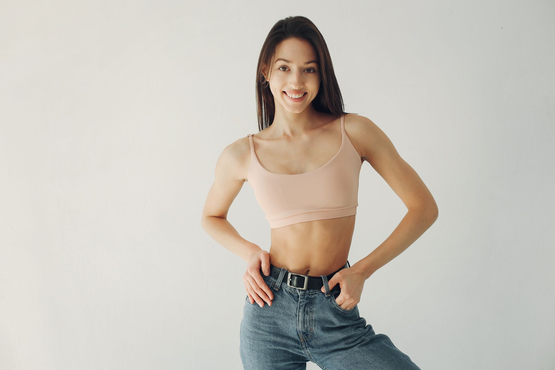 A woman in a crop top and jeans is standing with her hands in her pockets.