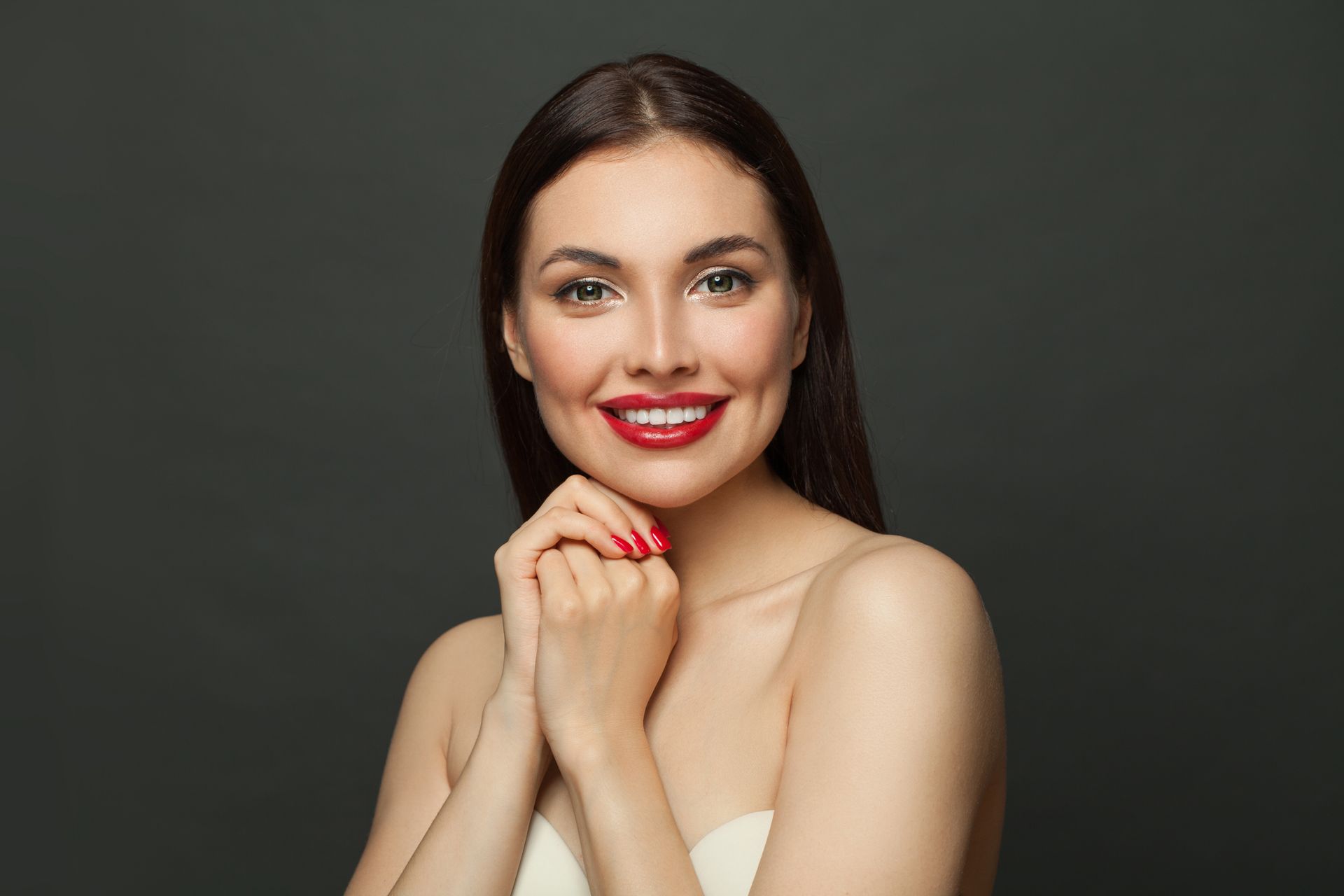 A beautiful young woman with red lipstick and red nails is smiling.