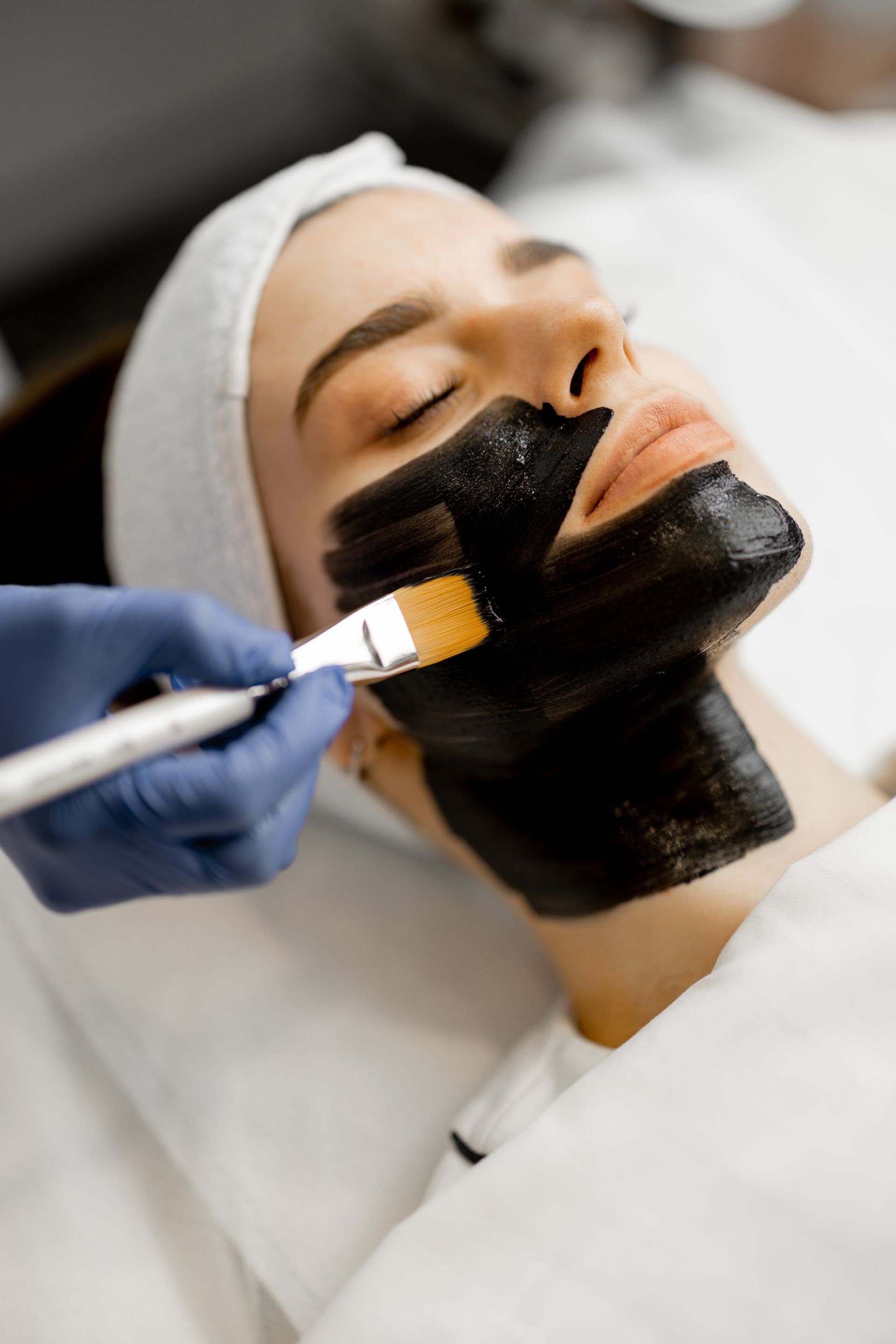 A woman is getting a black mask on her face.