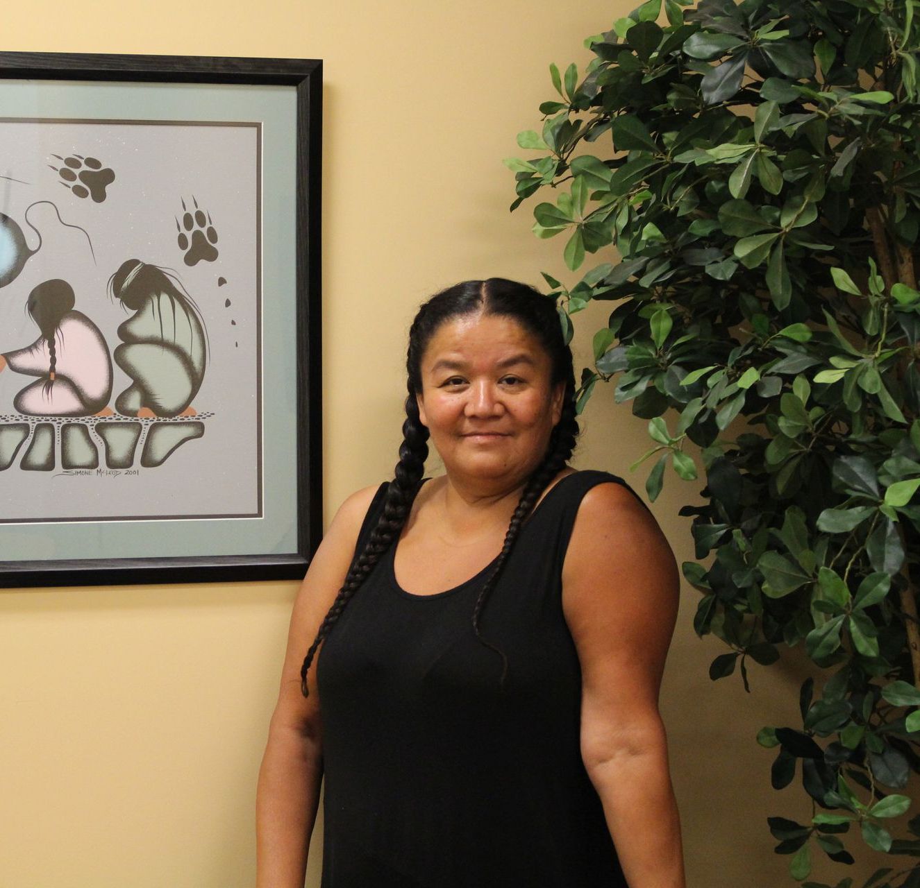 A woman in a black tank top stands in front of a framed picture