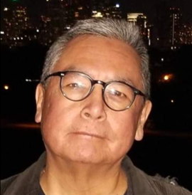 A man wearing glasses is standing in front of a city at night.