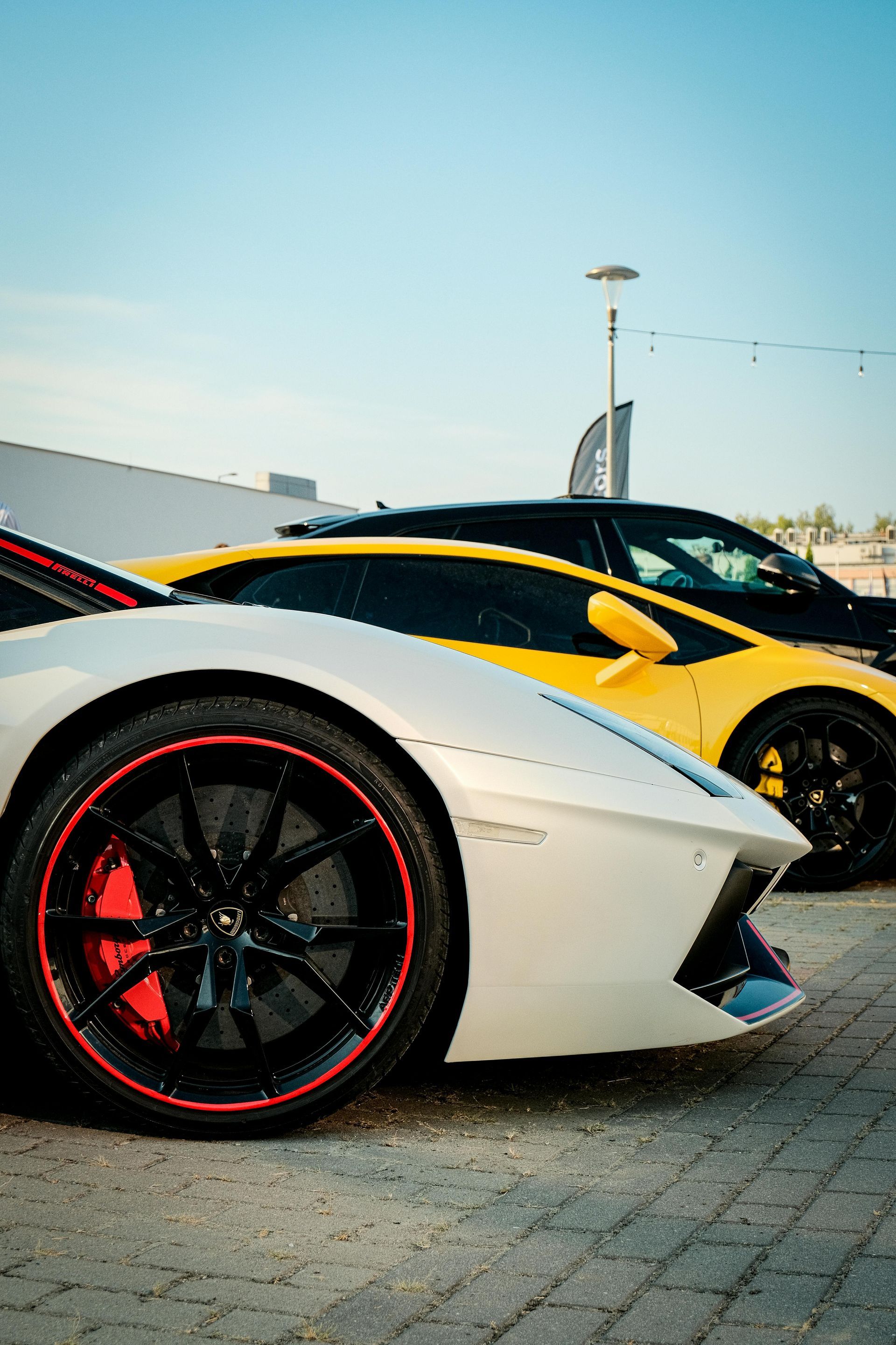 White and yellow sports cars parked outdoors with a blue sky background.