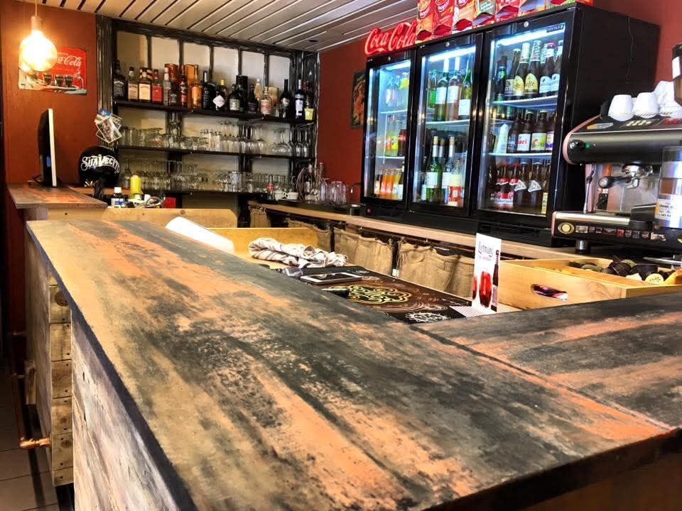 Interno rustico del bar con bancone in legno, scaffali per liquori e refrigeratori per bevande illuminati di rosso.