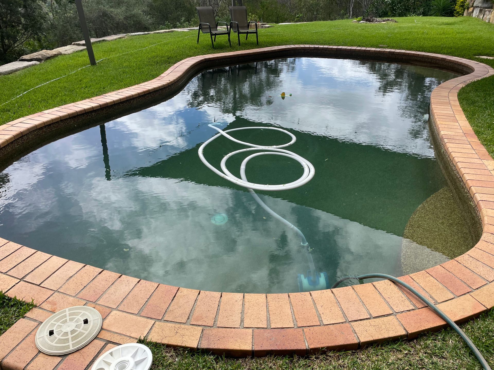 Oval-shaped Swimming Pool With Brick Edging. A Hose and Cleaner Are Inside the Pool — Leak N Pool In Logan, QLD