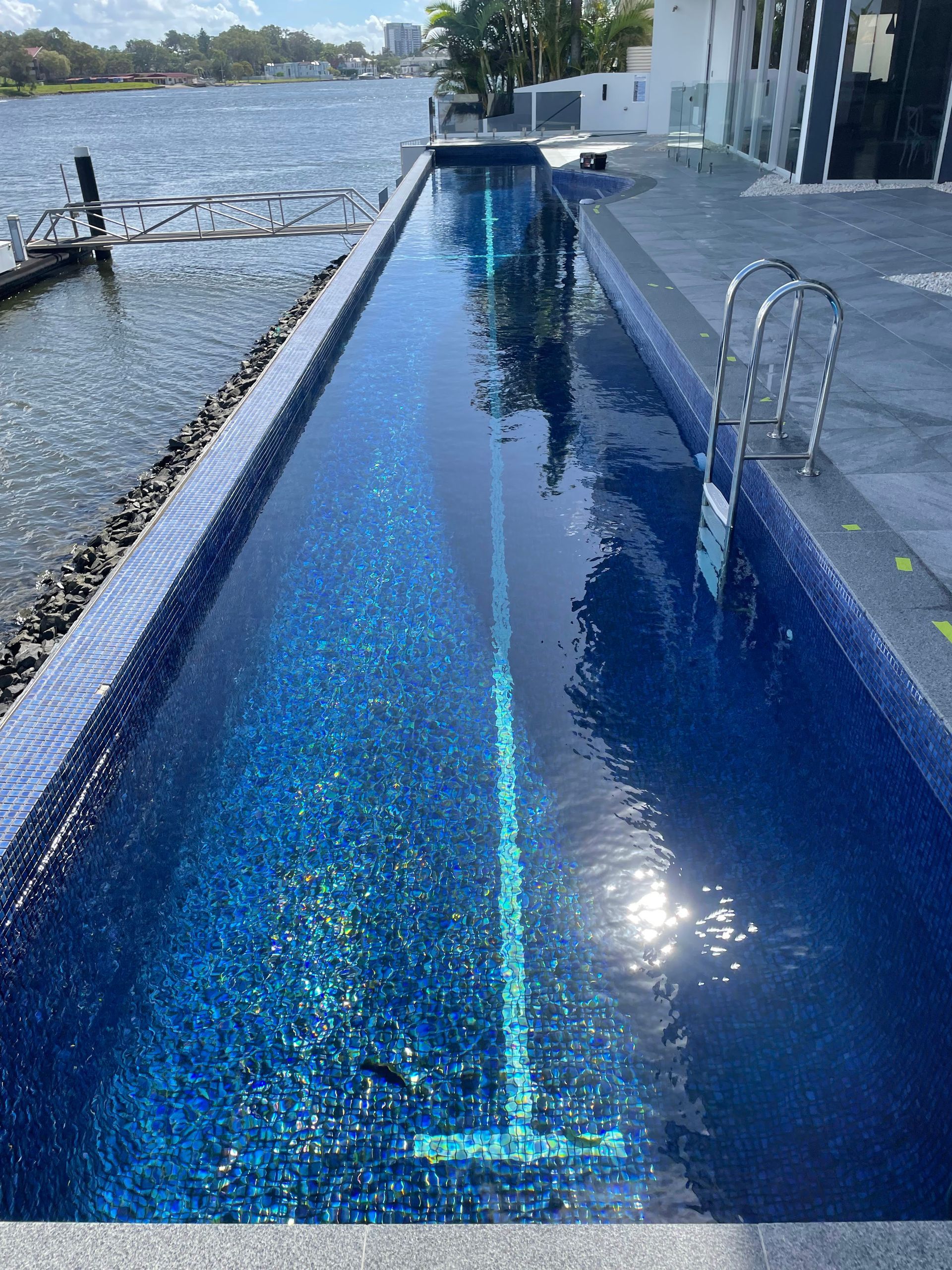 Long, Narrow Swimming Pool With Blue Tiles, Next to a Waterfront With a Dock — Leak N Pool In Southport, QLD