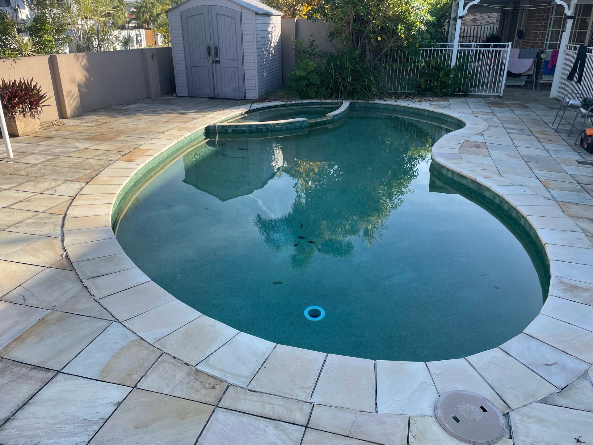 Swimming Pool With Light Stone Surround. A Small Shed and Fence Are in the Background — Leak N Pool In Southport, QLD