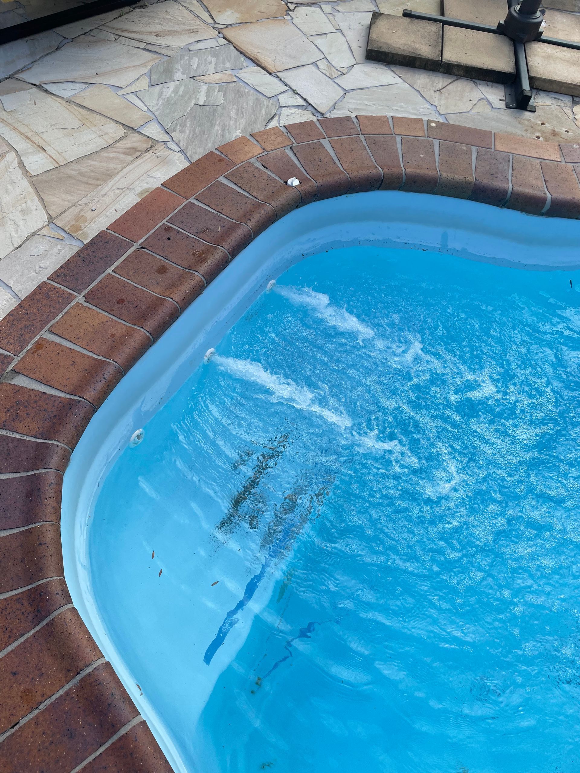 Corner of a Blue Swimming Pool With Swirling Water, Brick Border, and Stone Patio — Leak N Pool In Southport, QLD