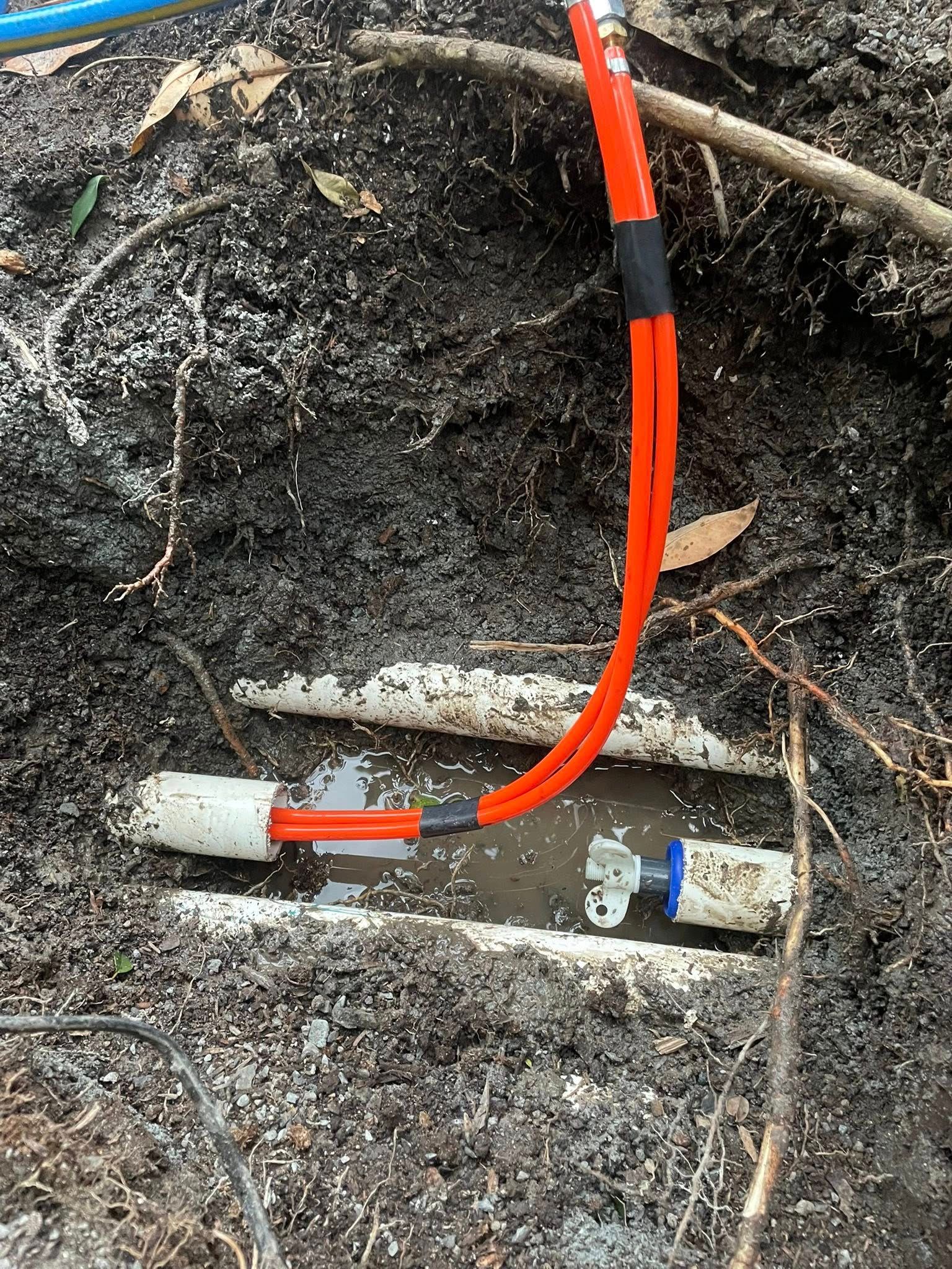 Pipes and Fittings in a Small Dirt Trench, With Orange Tubing and Blue Connector — Leak N Pool In Logan, QLD
