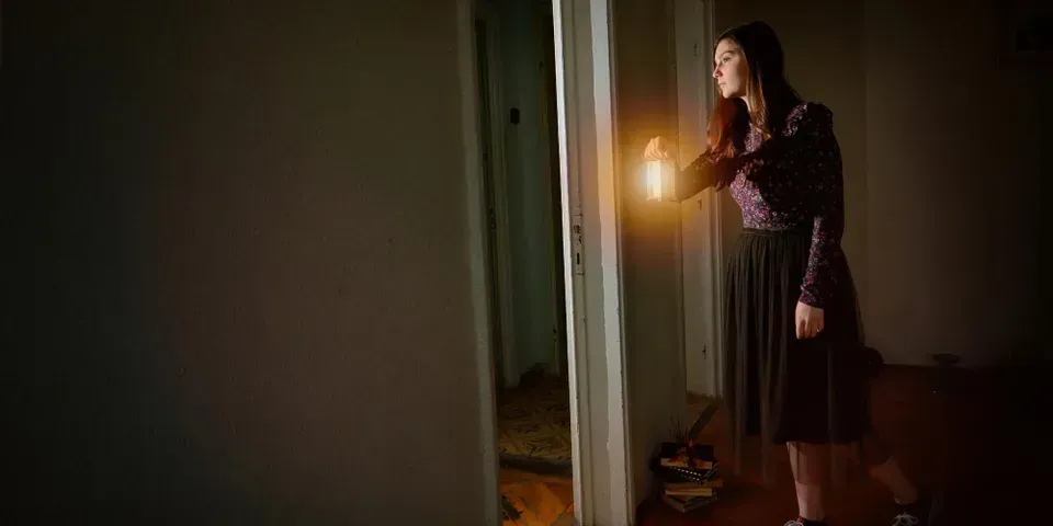 A young lady walking inside the house in the dark holding a lamp