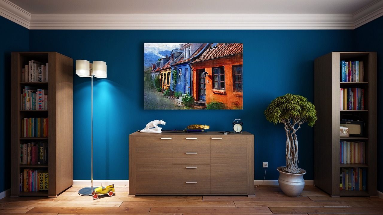 A room with a dark blue wall, a brown wooden dresser, a plant, a lamp, and a bookshelf. 