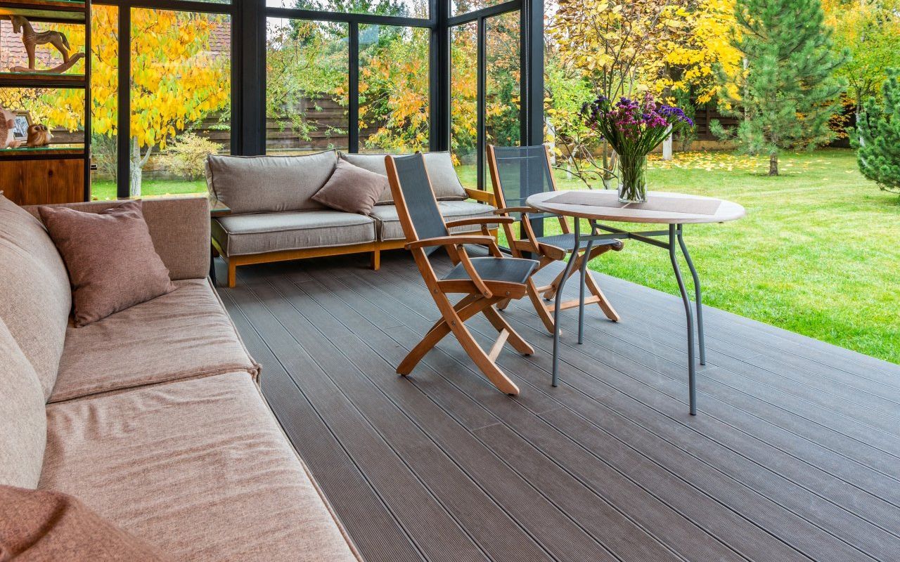 An outdoor patio with wooden chairs, a couch, and a table overlooking a backyard full of nature.