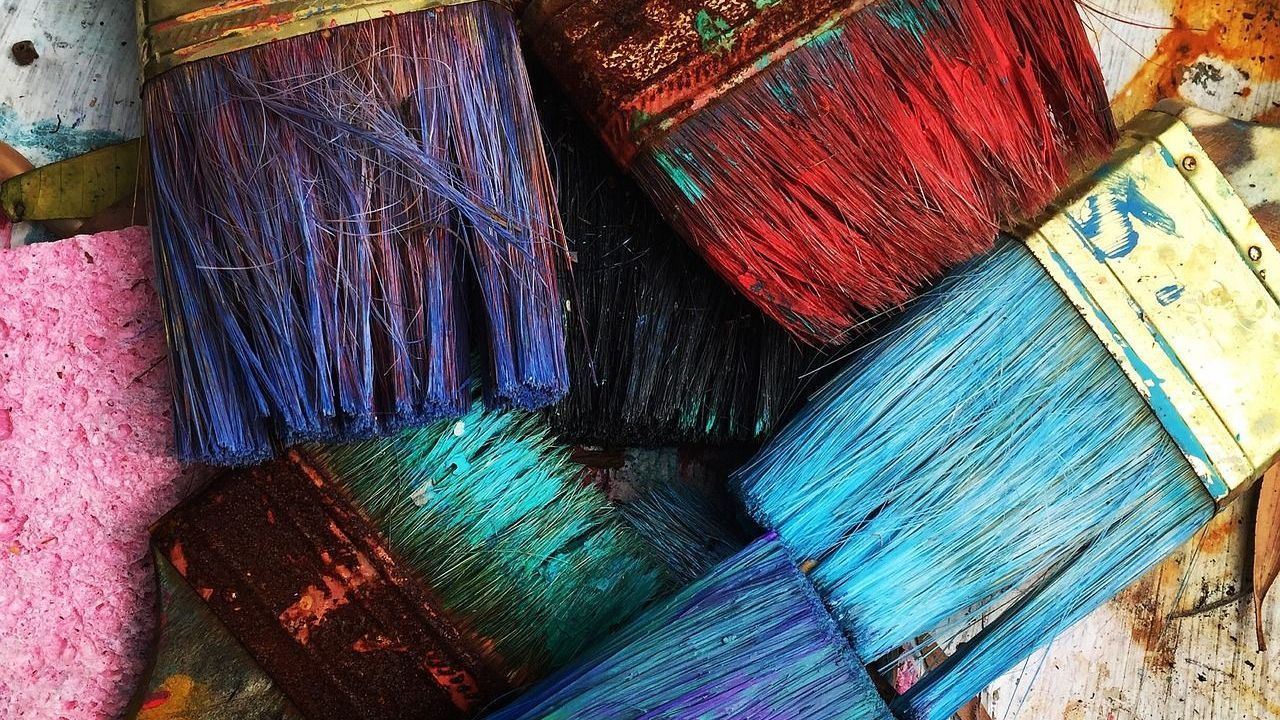 A picture of dirty paint brushes with multiple colors.