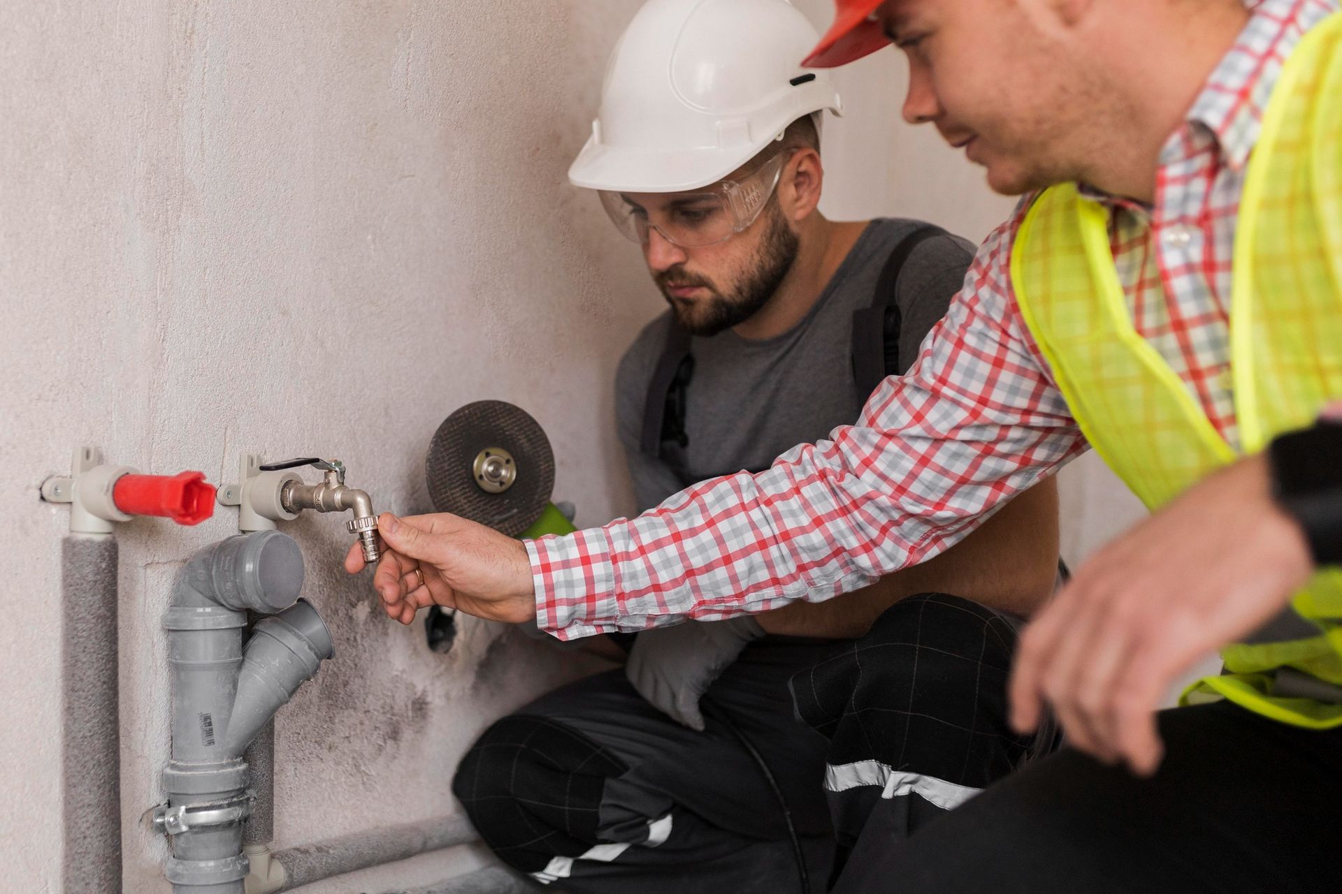 Two men are working on a pipe in a bathroom.