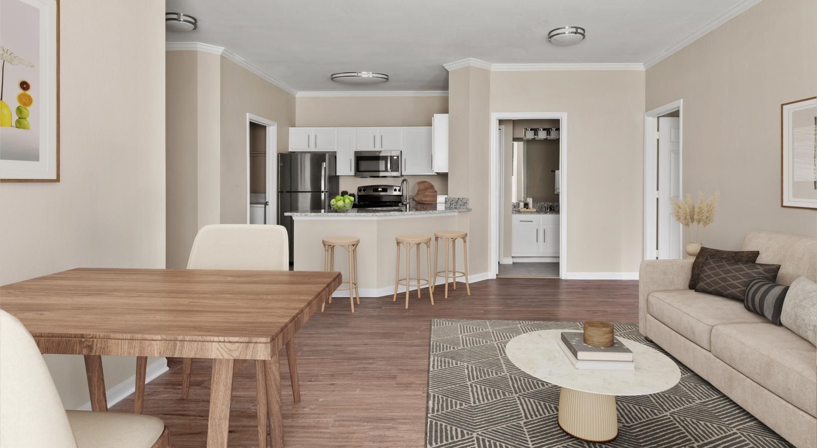 A bright open-concept apartment with a living room, dining area, and kitchen featuring light walls and wood floors.