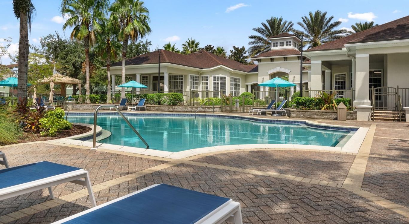 Empty blue lounge chairs arranged by a swimming pool, shaded by several turquoise and navy umbrellas.