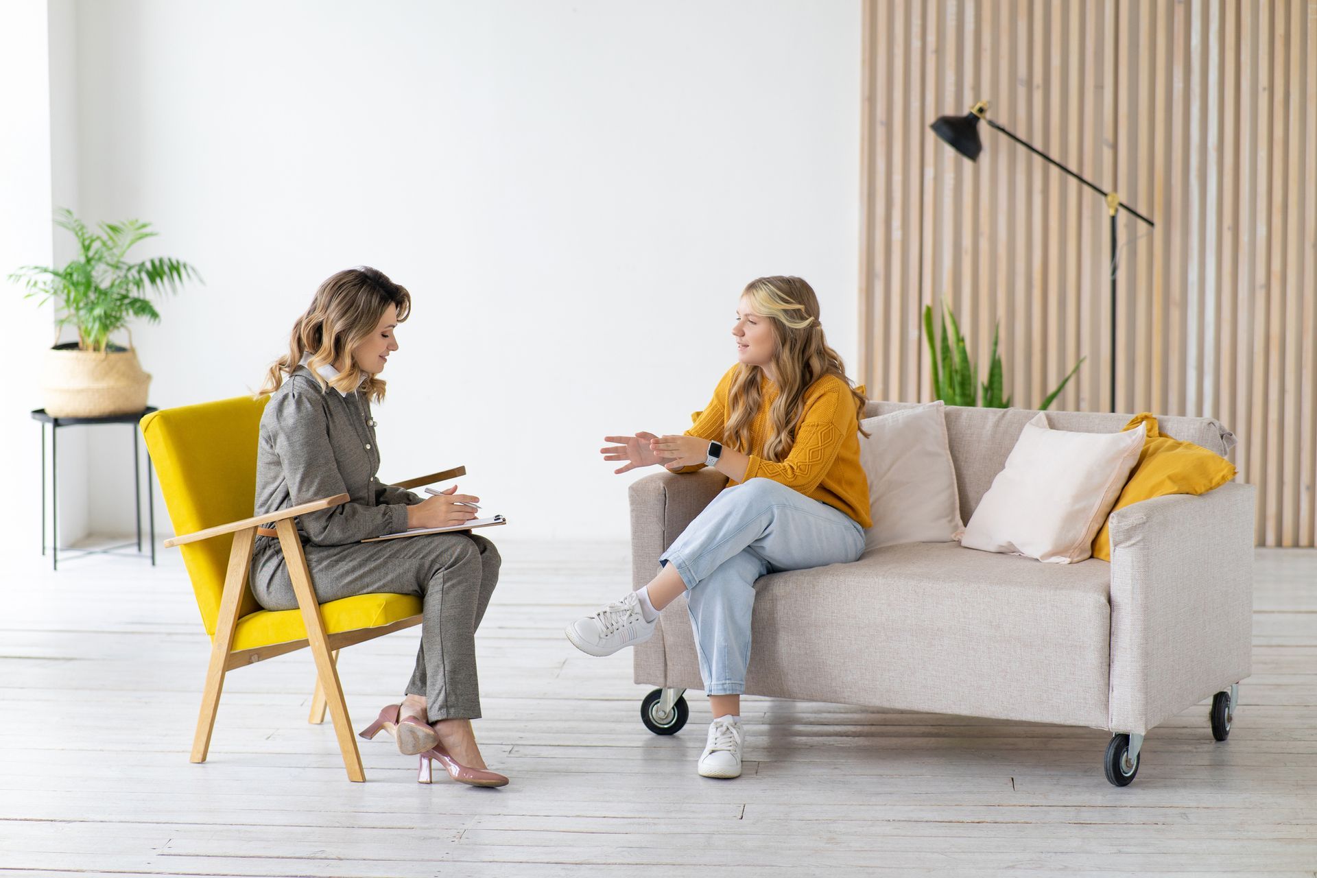 A woman is sitting on a couch talking to another woman.