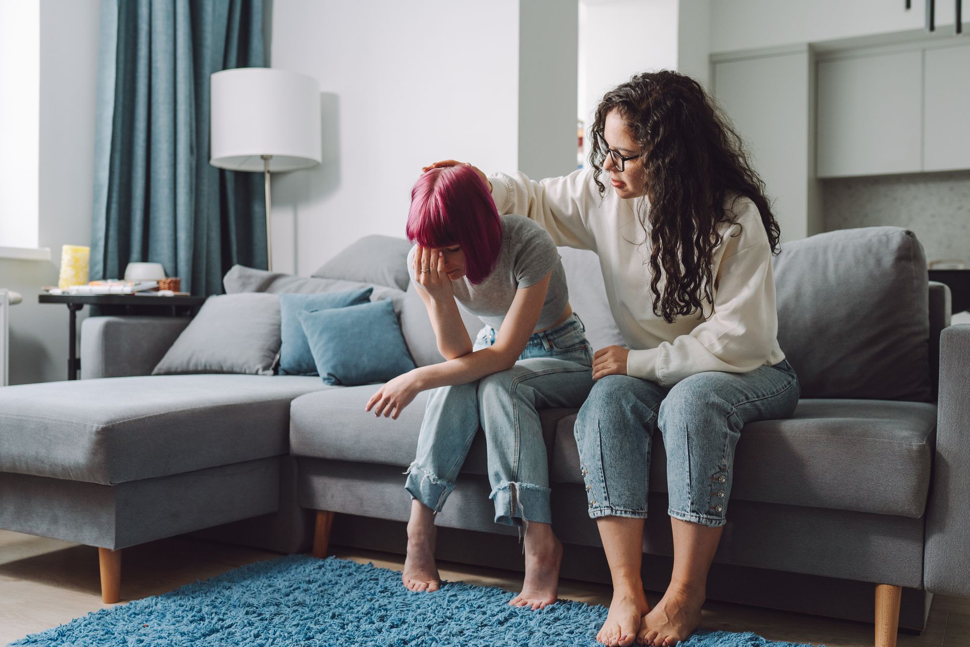 A woman is comforting another woman who is sitting on a couch.