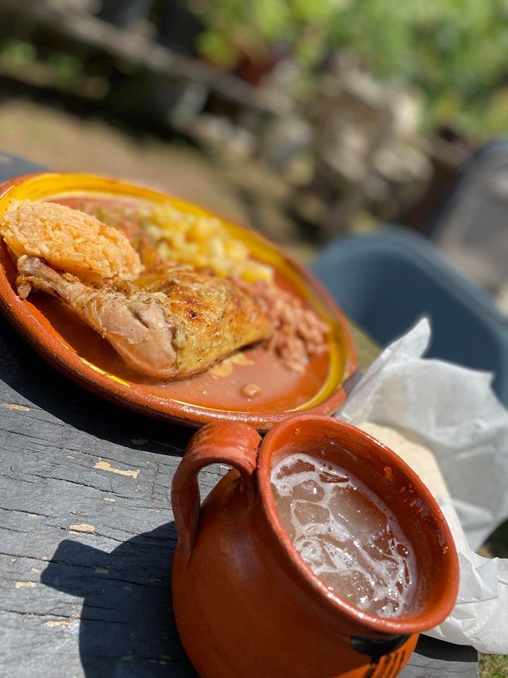 Plate of roasted chicken, beans, and potatoes with a mug of drink on a wooden table.