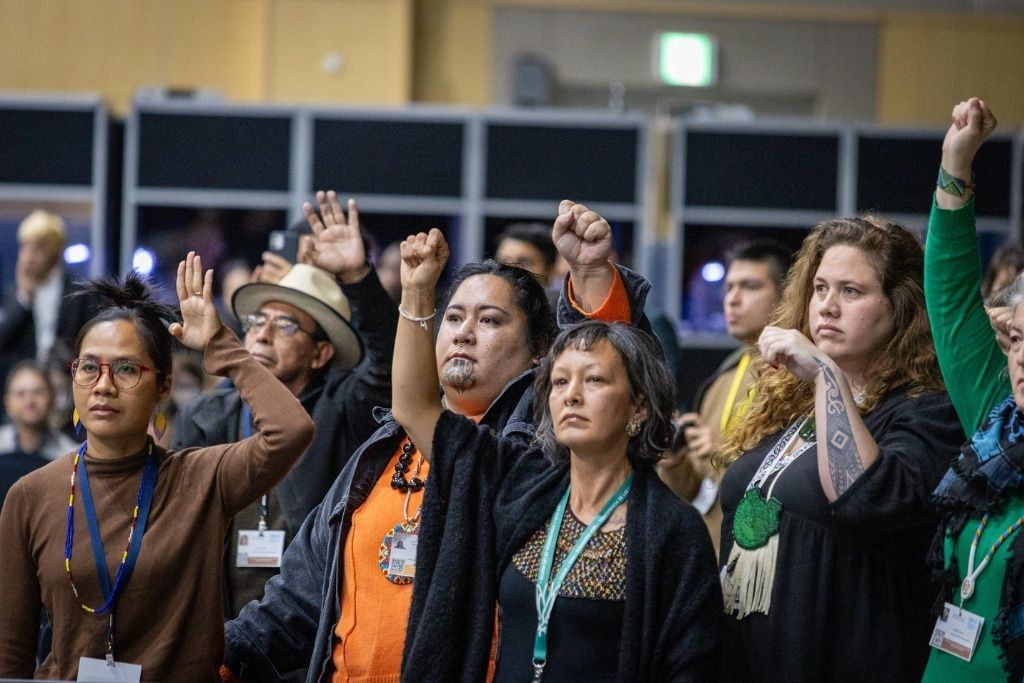 People with fists raised in the air, a show of solidarity. Indoor setting.