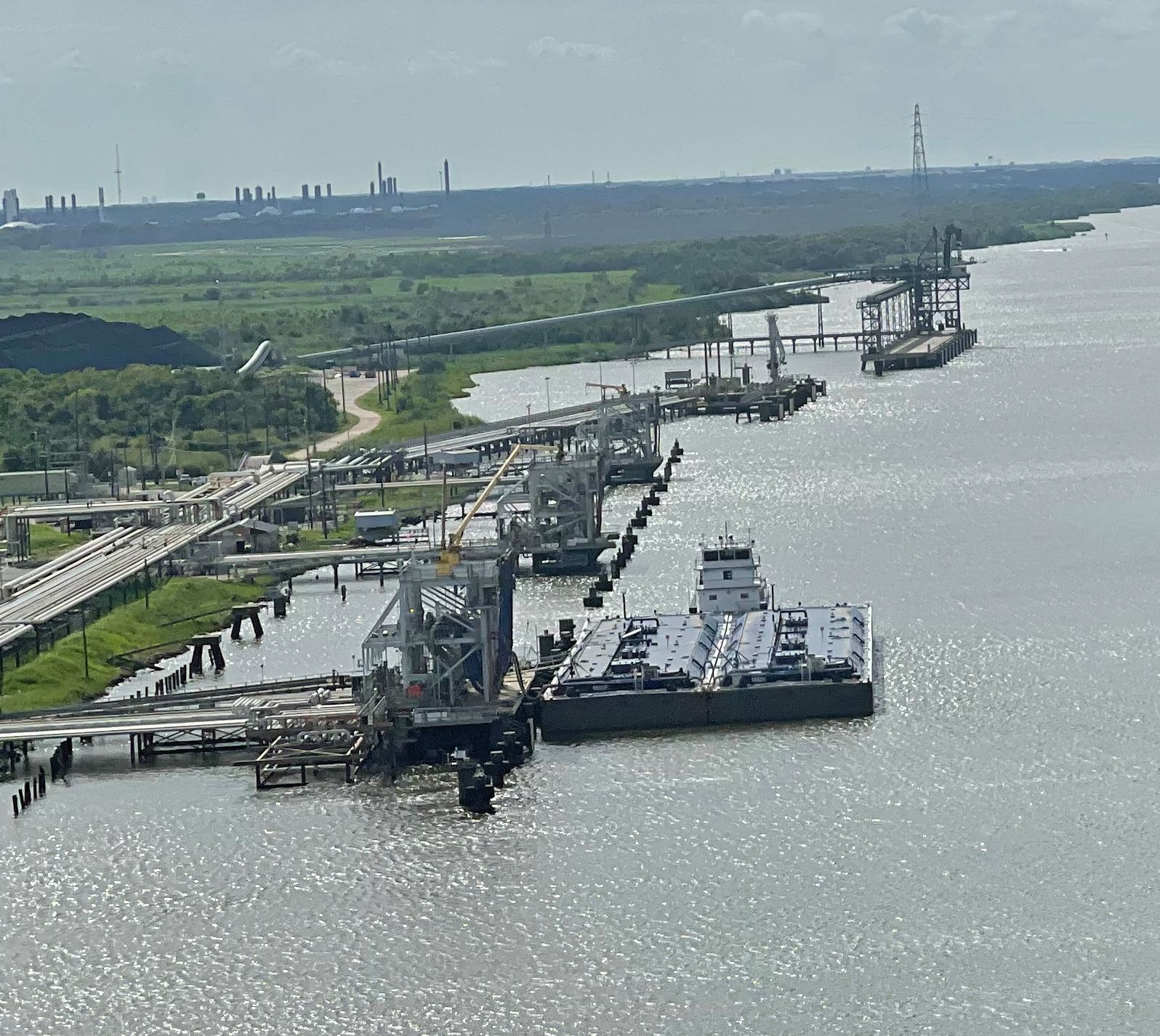 A river scene with a bridge, industrial area, and barge in the foreground.