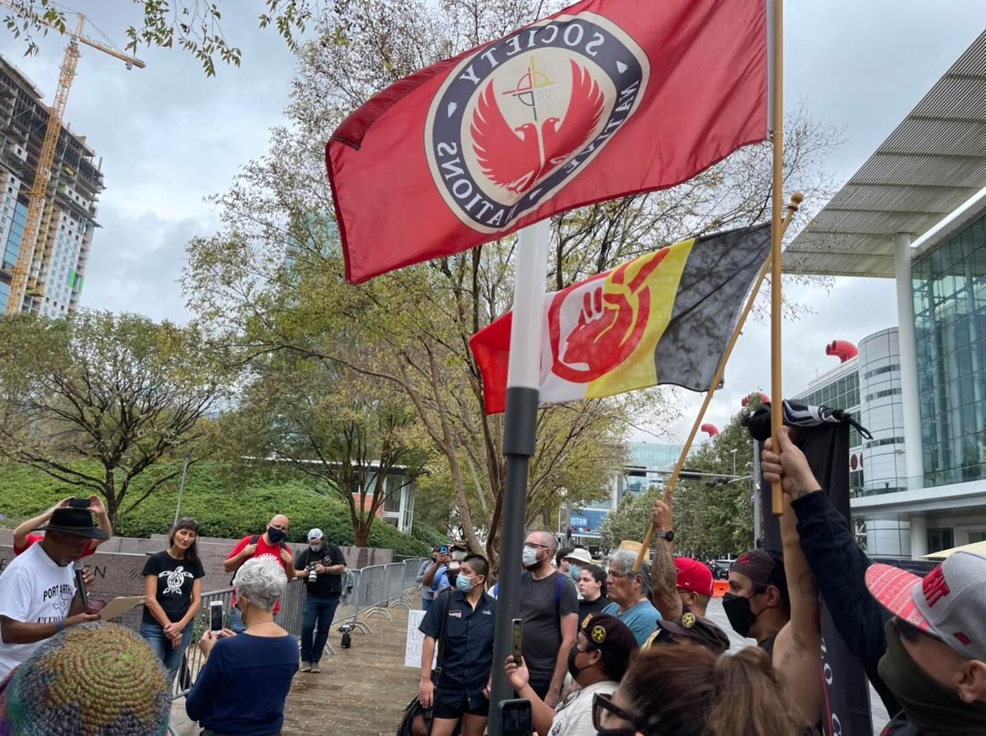 Protesters waving flags, red phoenix, clenched fist, gathering outdoors near buildings.
