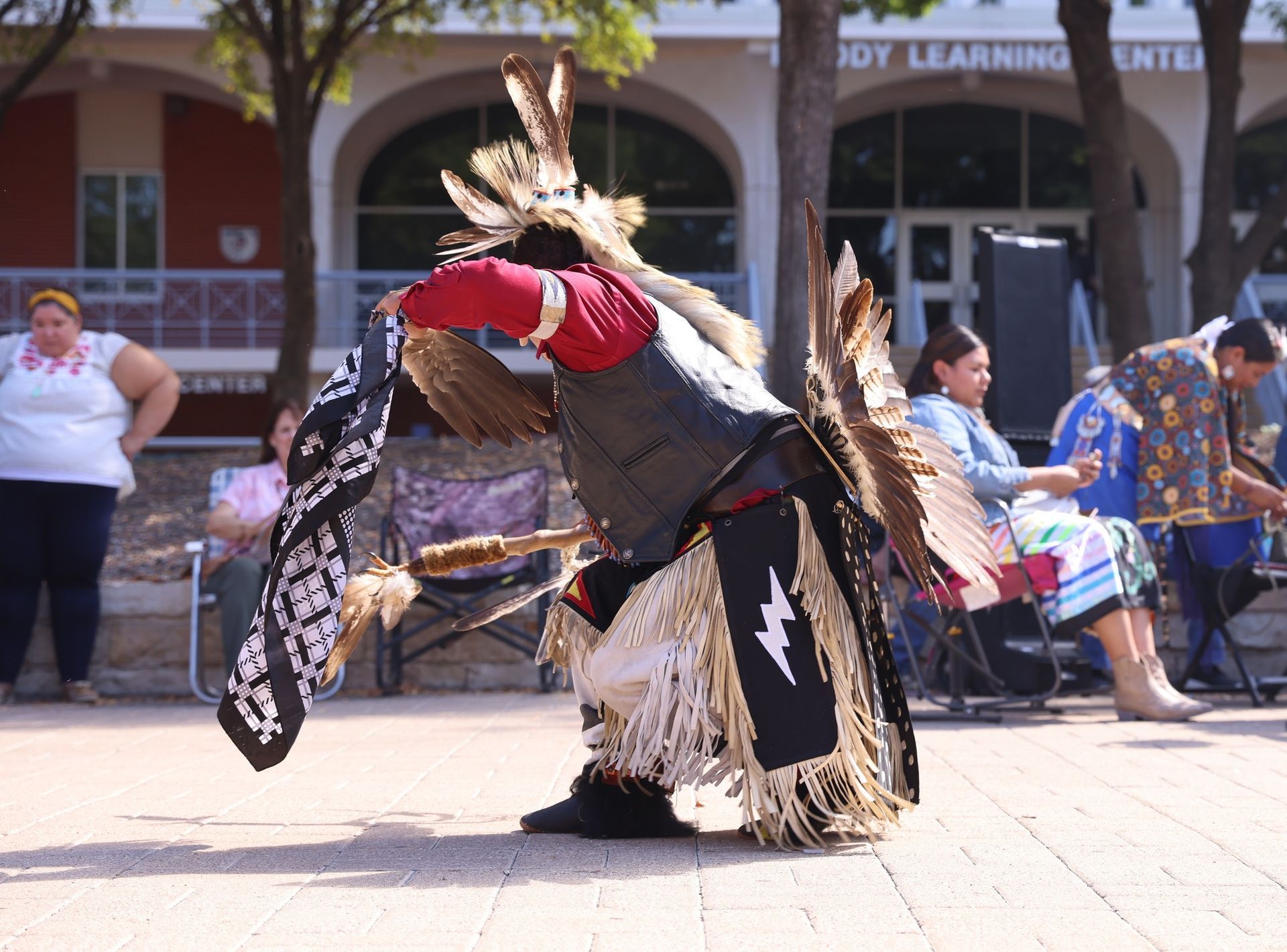 Indigenous people march in a city, holding signs and flags, protesting. Bright sunny day.