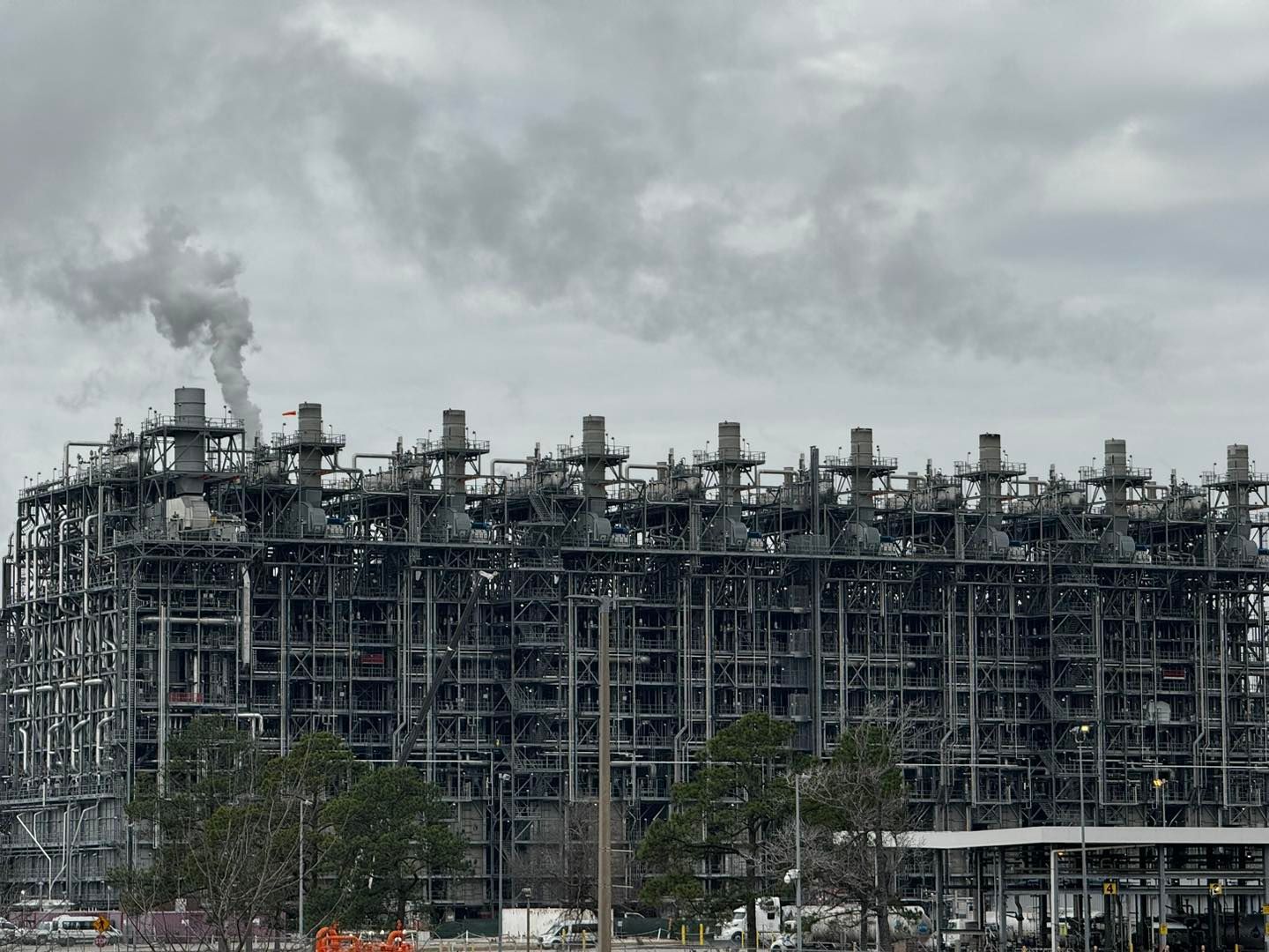 Industrial complex with many pipes and smokestacks releasing smoke into the gray sky.