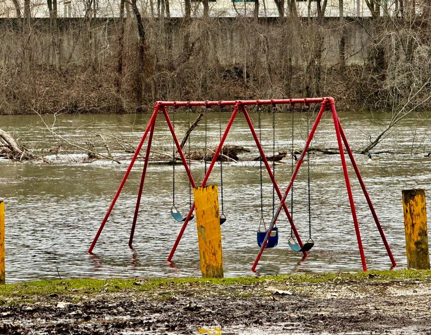 Red swing set submerged in floodwater.