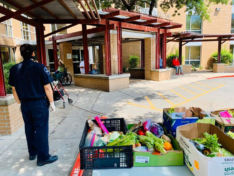 Person in uniform stands by crates of fresh produce outside a building.