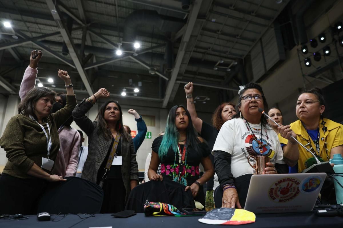 Group of people with fists raised, some speaking at a table; event inside.