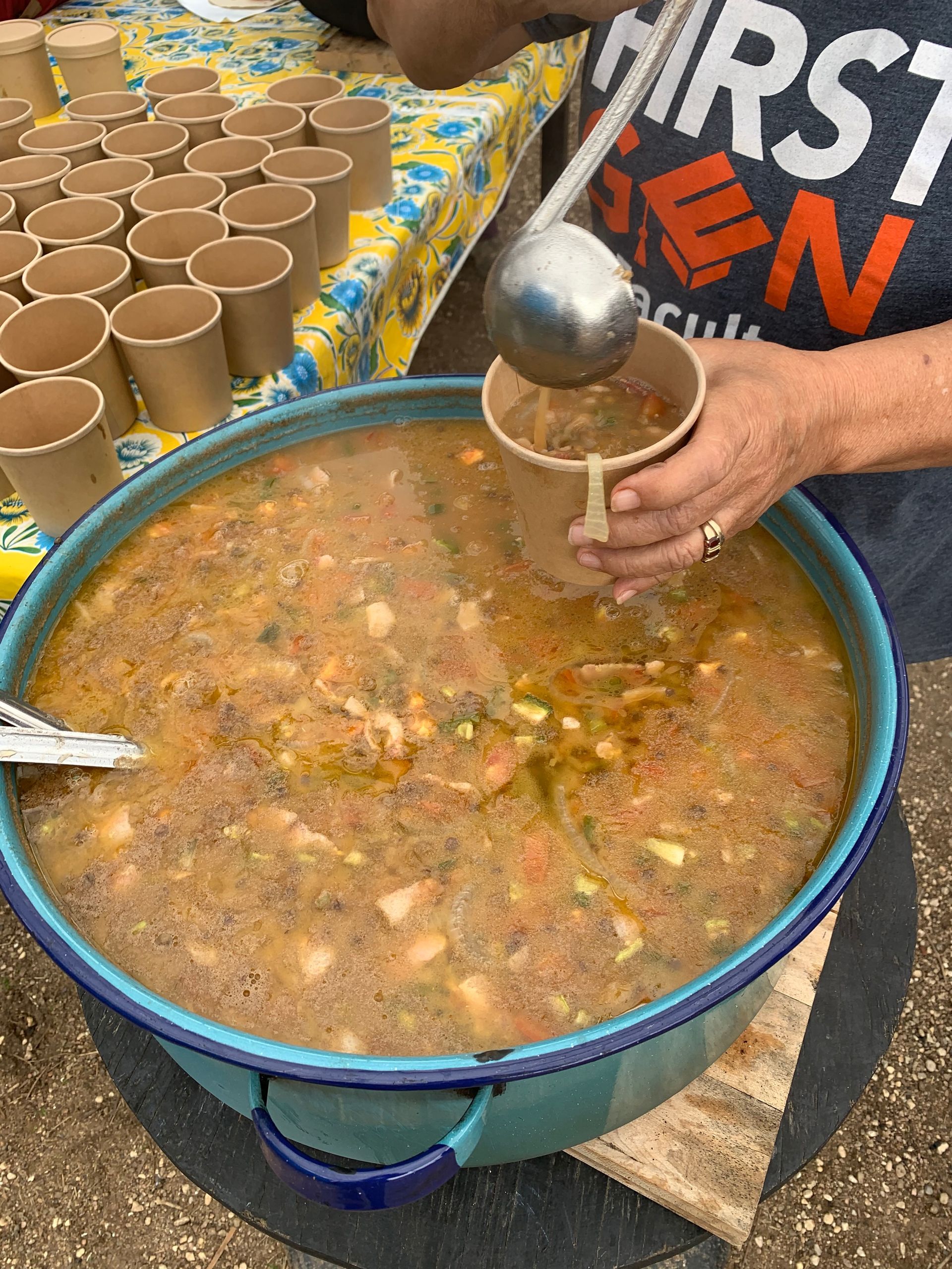 A person ladles soup from a large pot into paper cups at an outdoor event.