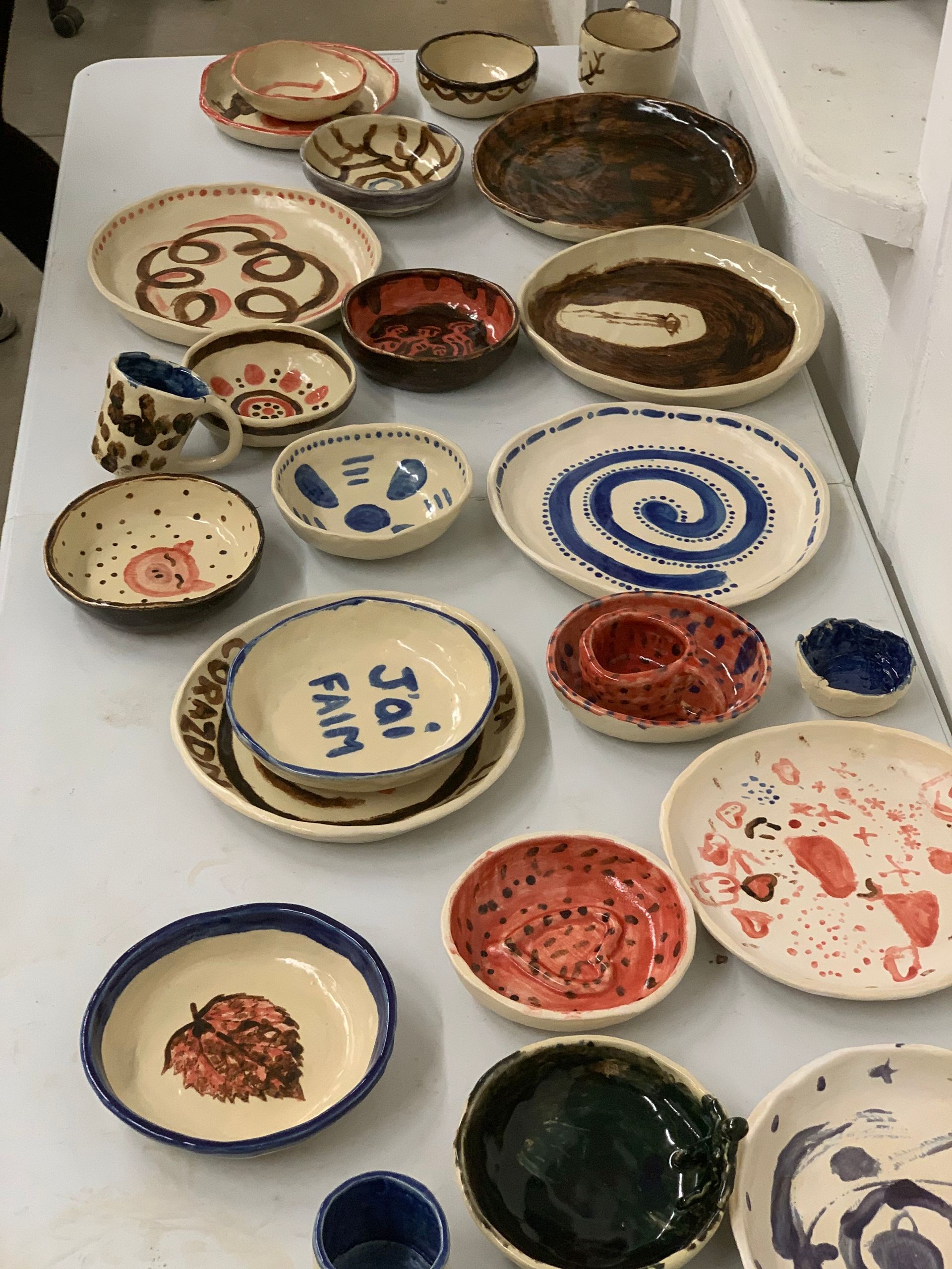 Various handmade ceramic plates and bowls in different sizes and colorful designs on a white table.