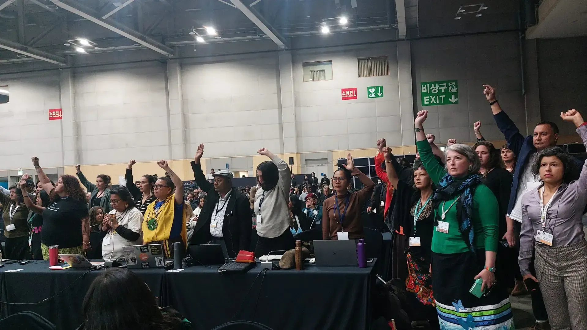People raising fists in solidarity at a conference. Indoors, bright lighting, diverse attire.