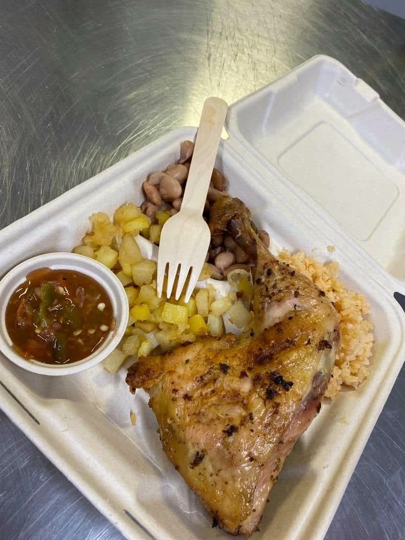 Grilled chicken leg meal with salsa, corn, beans, rice, and a wooden fork.