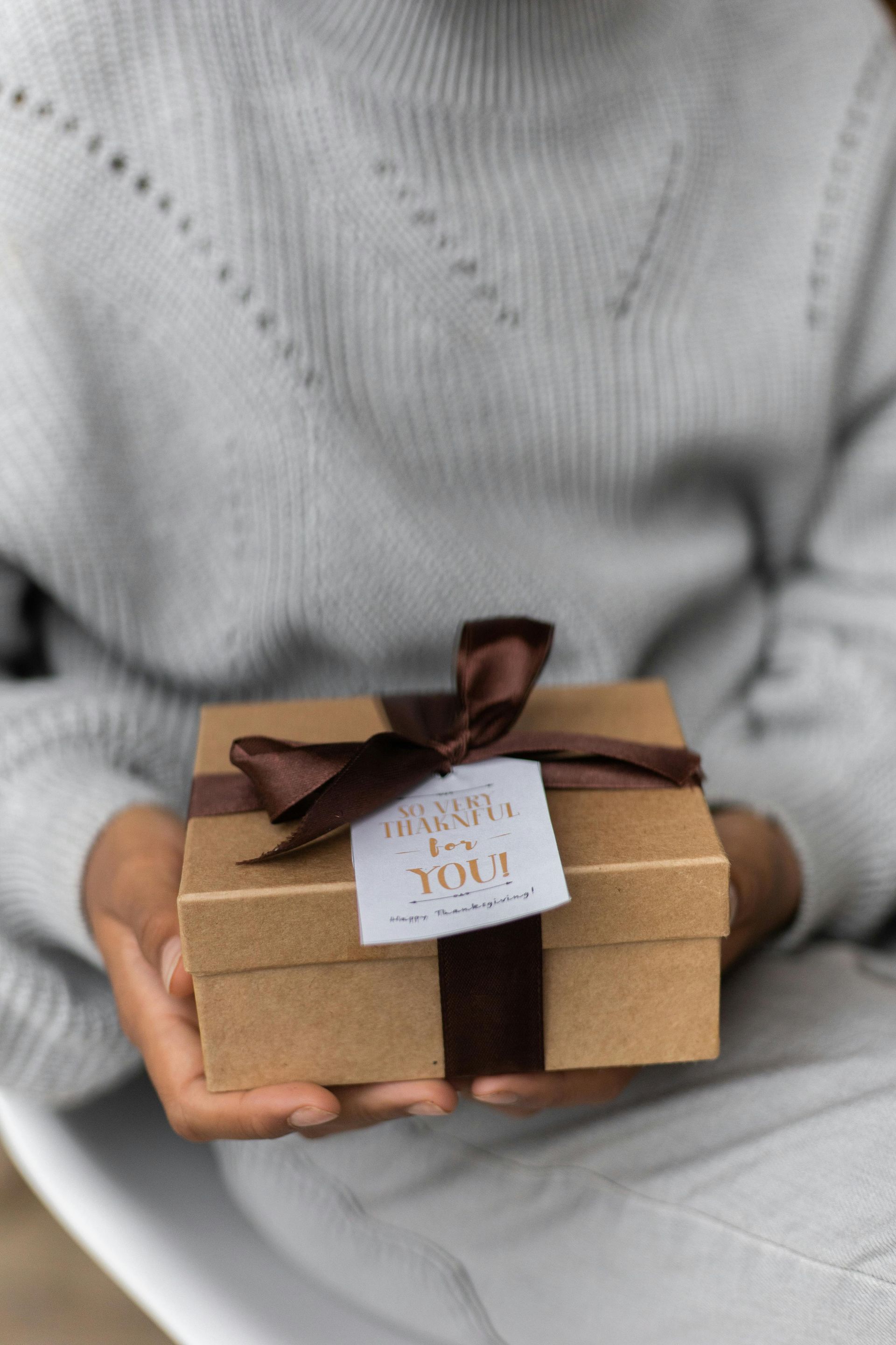 A person is holding a small gift box with a tag that says thank you