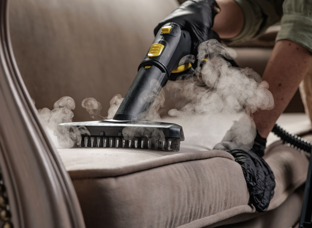 Steam cleaner sanitizing a beige couch with a black brush attachment