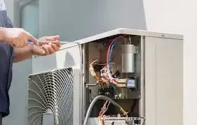 Person repairing an air conditioning unit; wires exposed, open panel, outdoor setting.