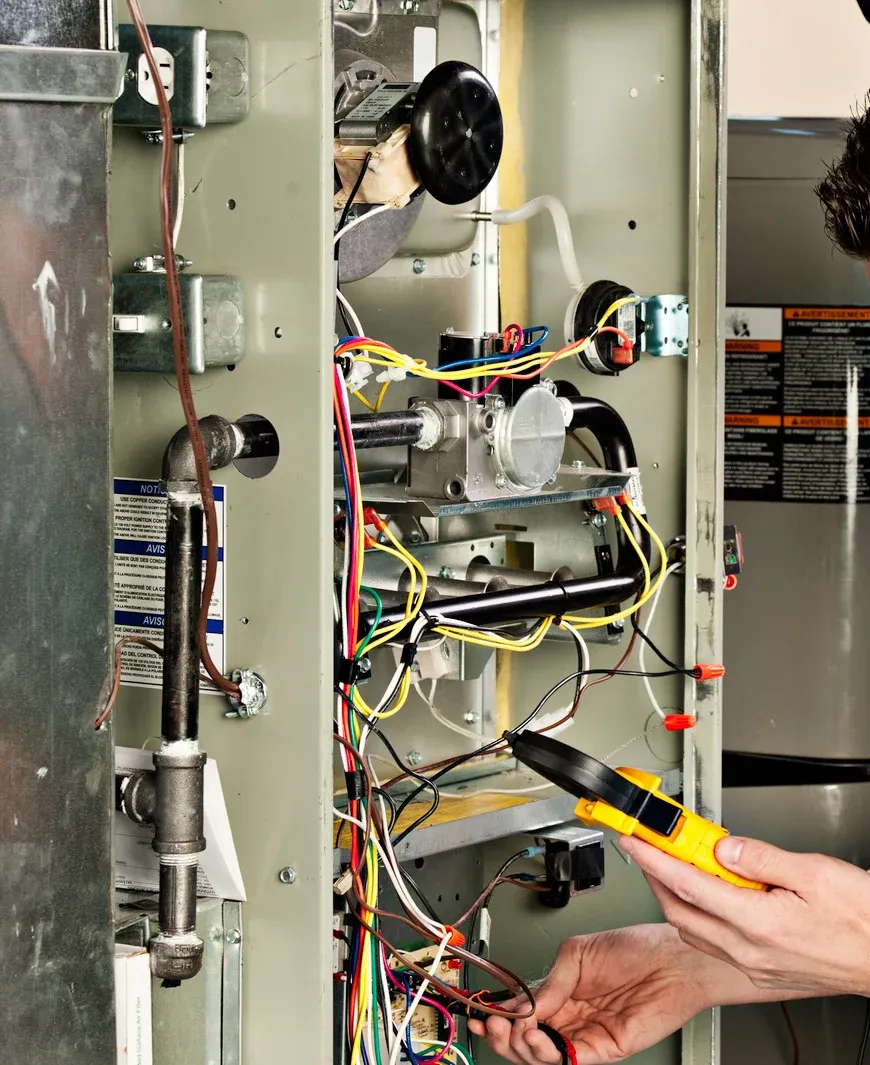 Person working on furnace wiring with yellow pliers inside open metal panel.
