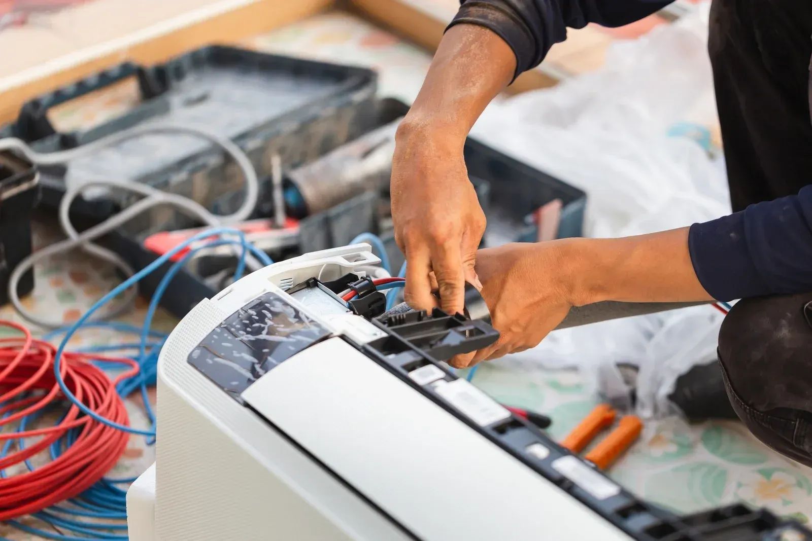 Person repairing an air conditioner; hands working with wires and tools, close-up.