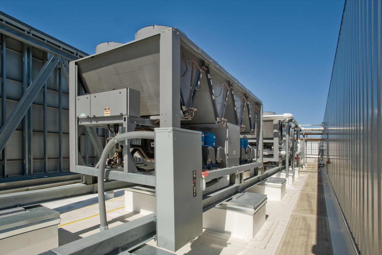 Rooftop chillers on a commercial building under a clear blue sky.