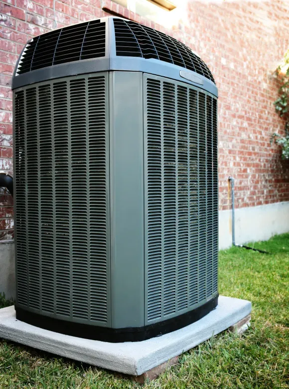 Central air conditioning unit on a concrete pad near a brick wall.