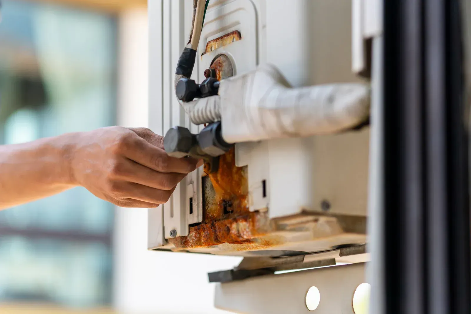 Person inspecting corroded, rusty white appliance with exposed pipes and fittings.