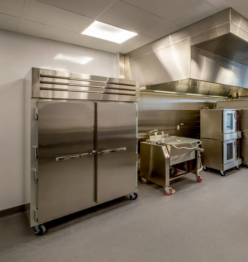 Commercial kitchen with stainless steel refrigerator, sink, and other equipment.