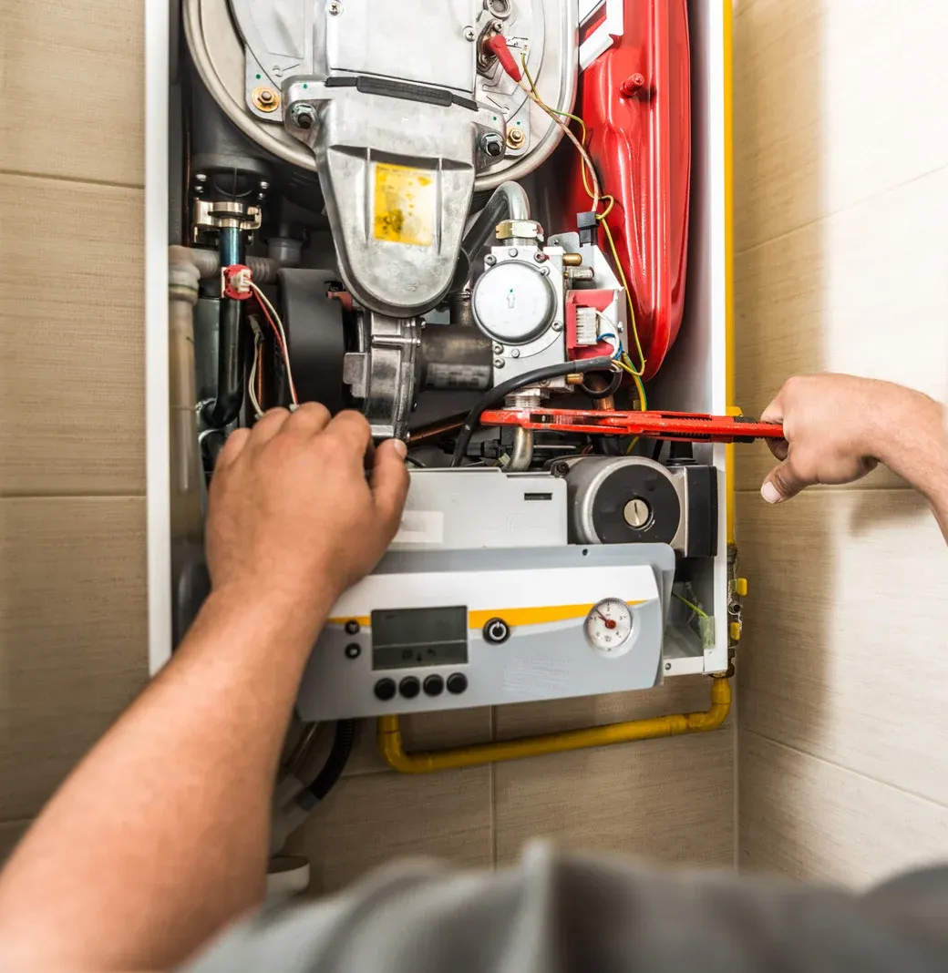 Person using a wrench to repair a gas boiler in a home.