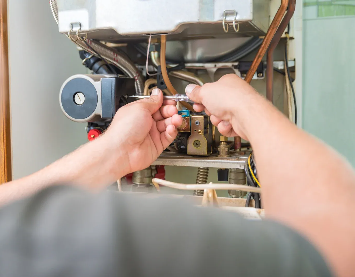 Person using a wrench to repair a boiler, indoors.