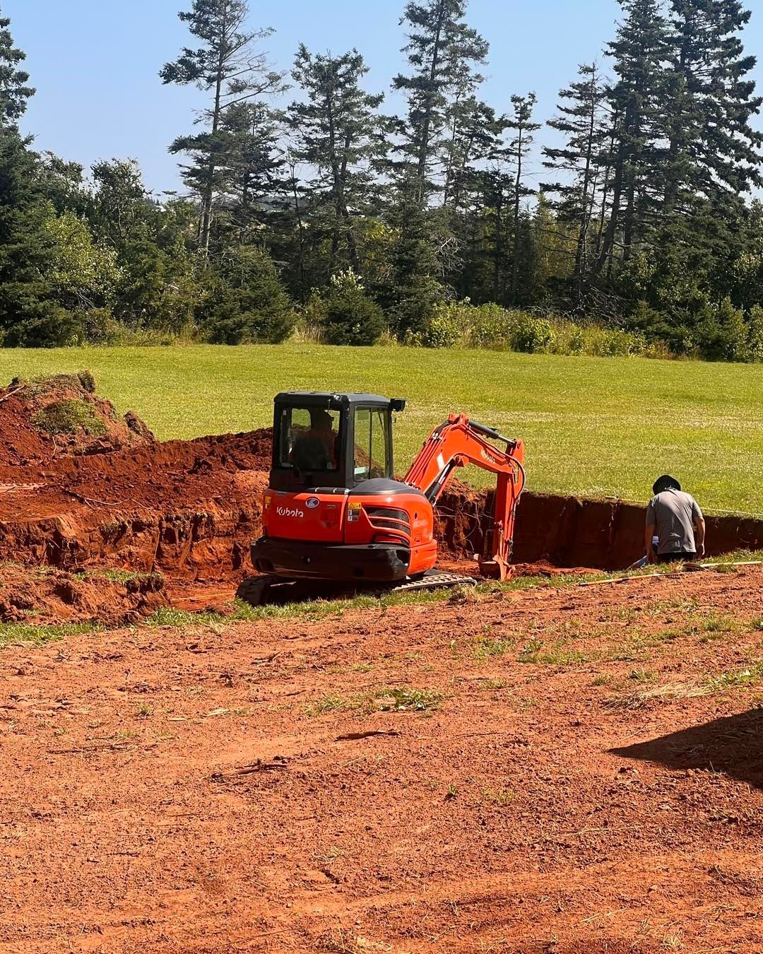 An orange excavator is digging a hole in the dirt in a field.