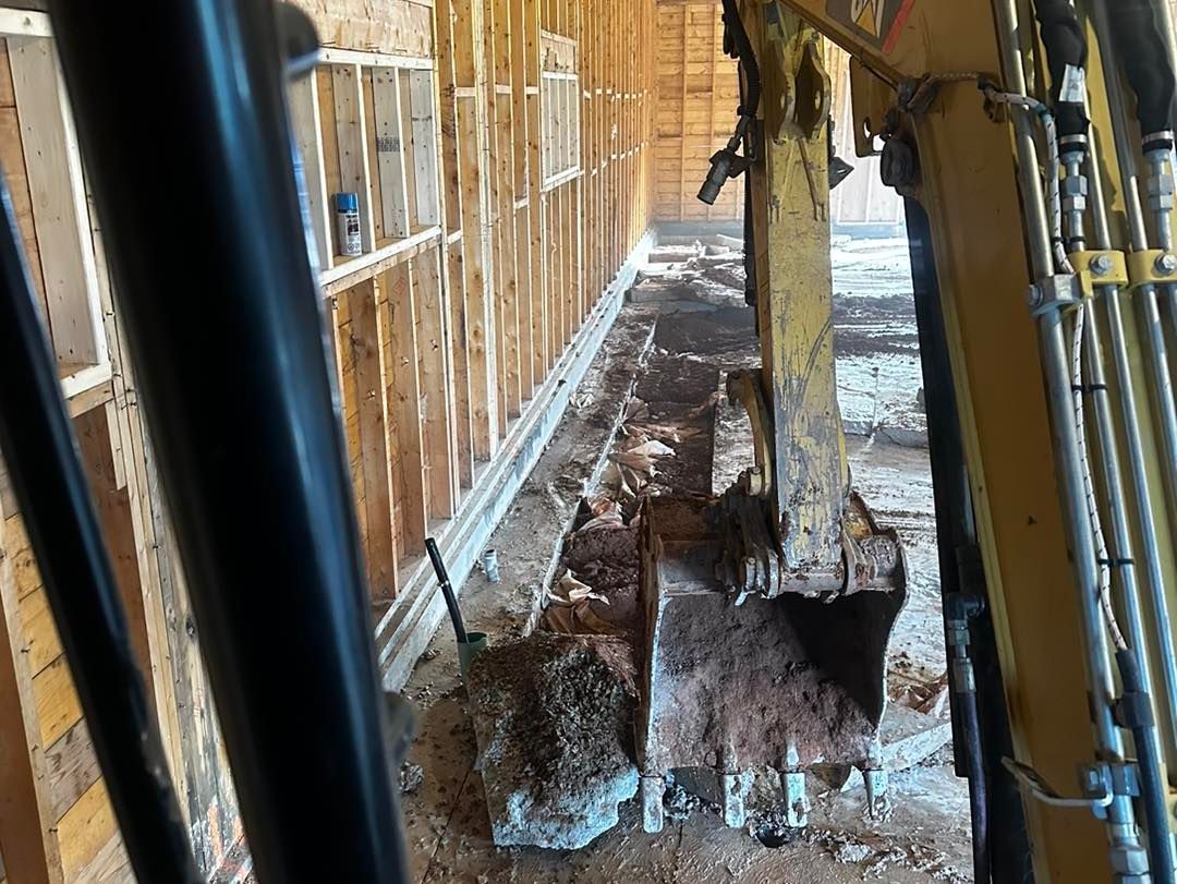 A yellow excavator is digging a hole in a building under construction.