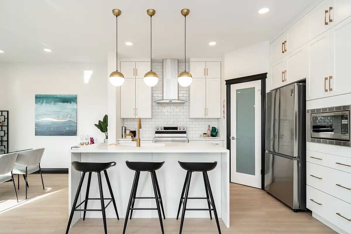A kitchen with white cabinets , stainless steel appliances , and a large island with three stools.
