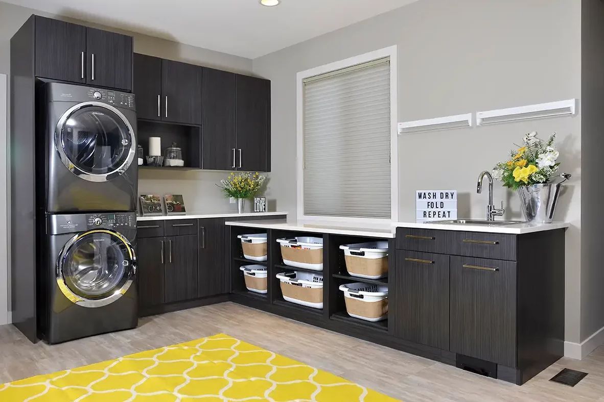 Laundry room with stacked washer/dryer, dark cabinets, yellow rug, and laundry baskets.