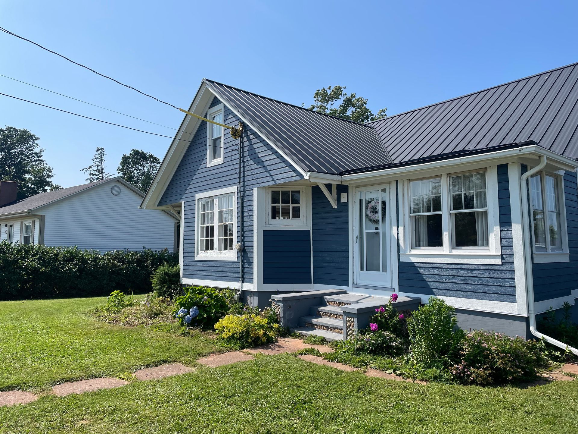 A blue house with white trim and a gray roof is sitting on top of a lush green lawn.